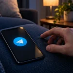 Официальный знак Telegram отображается на экране смартфона рядом с рукой пользователя