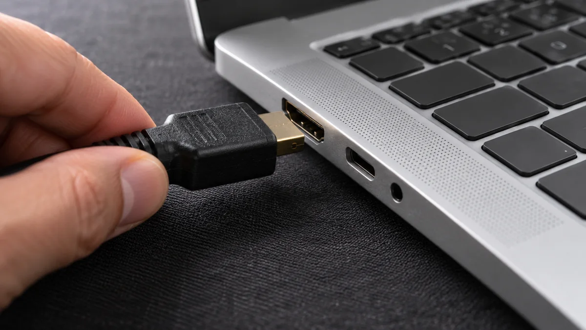 Рука подключает HDMI-кабель к боковому порту ноутбука